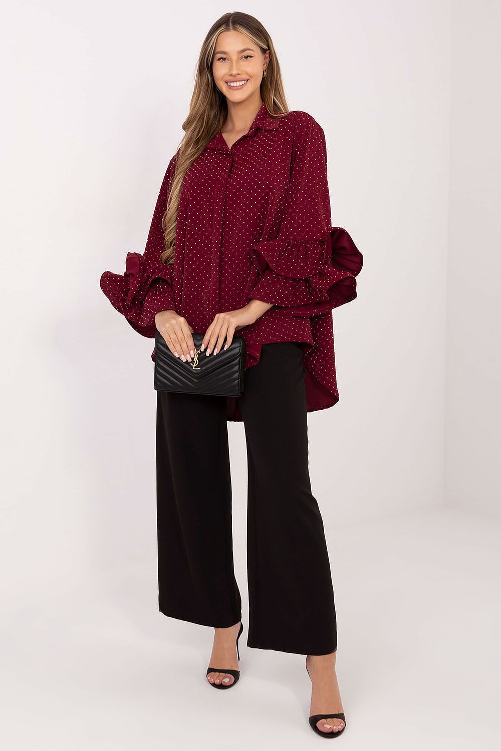 Woman wearing a burgundy oversized sweater with ruffled sleeves and black wide-leg pants on a white background.