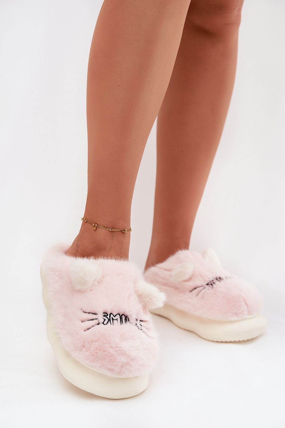 Pink fuzzy slippers with cat face design worn by a person on a white background