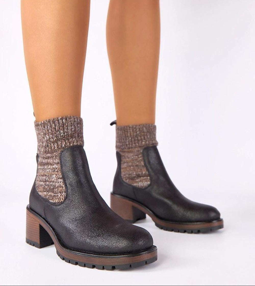 Black ankle boots with brown soles worn with patterned socks on a white background