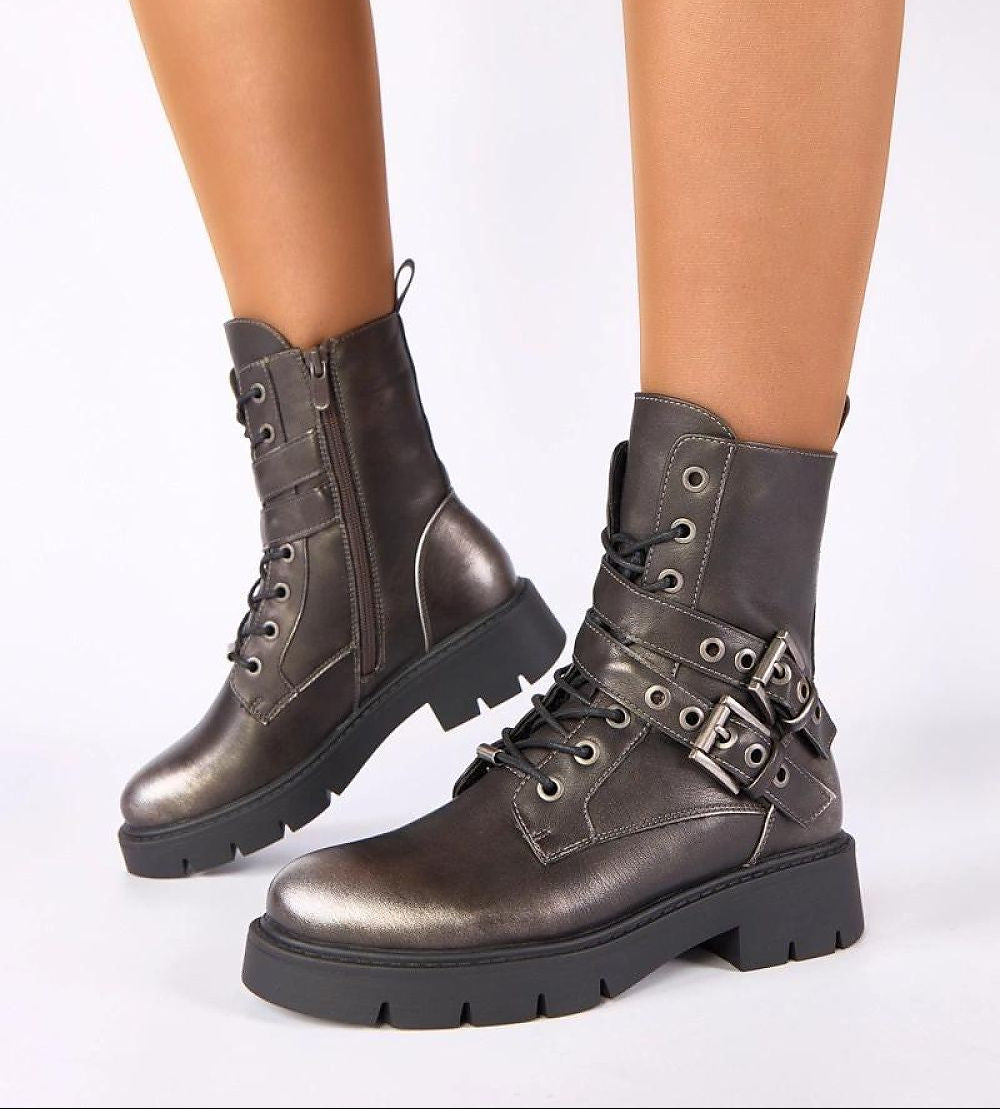 Gray combat boots with buckles worn by a person on a white background