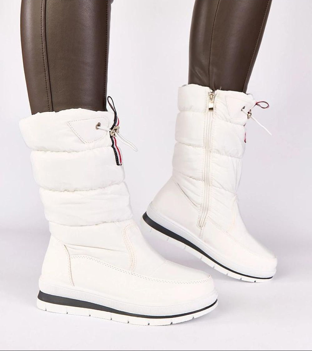 White winter boots with fur lining worn by a person in brown pants on a white background