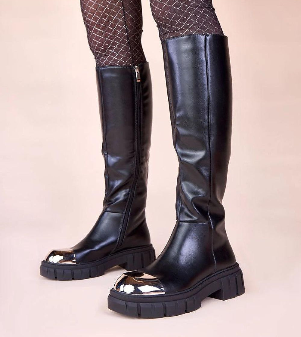 Black knee-high boots worn with patterned tights on a beige background