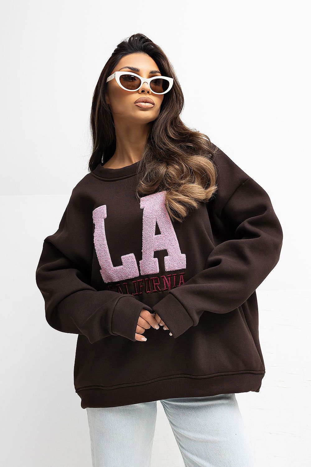 Woman wearing a brown sweatshirt with 'LA' printed on it against a white background