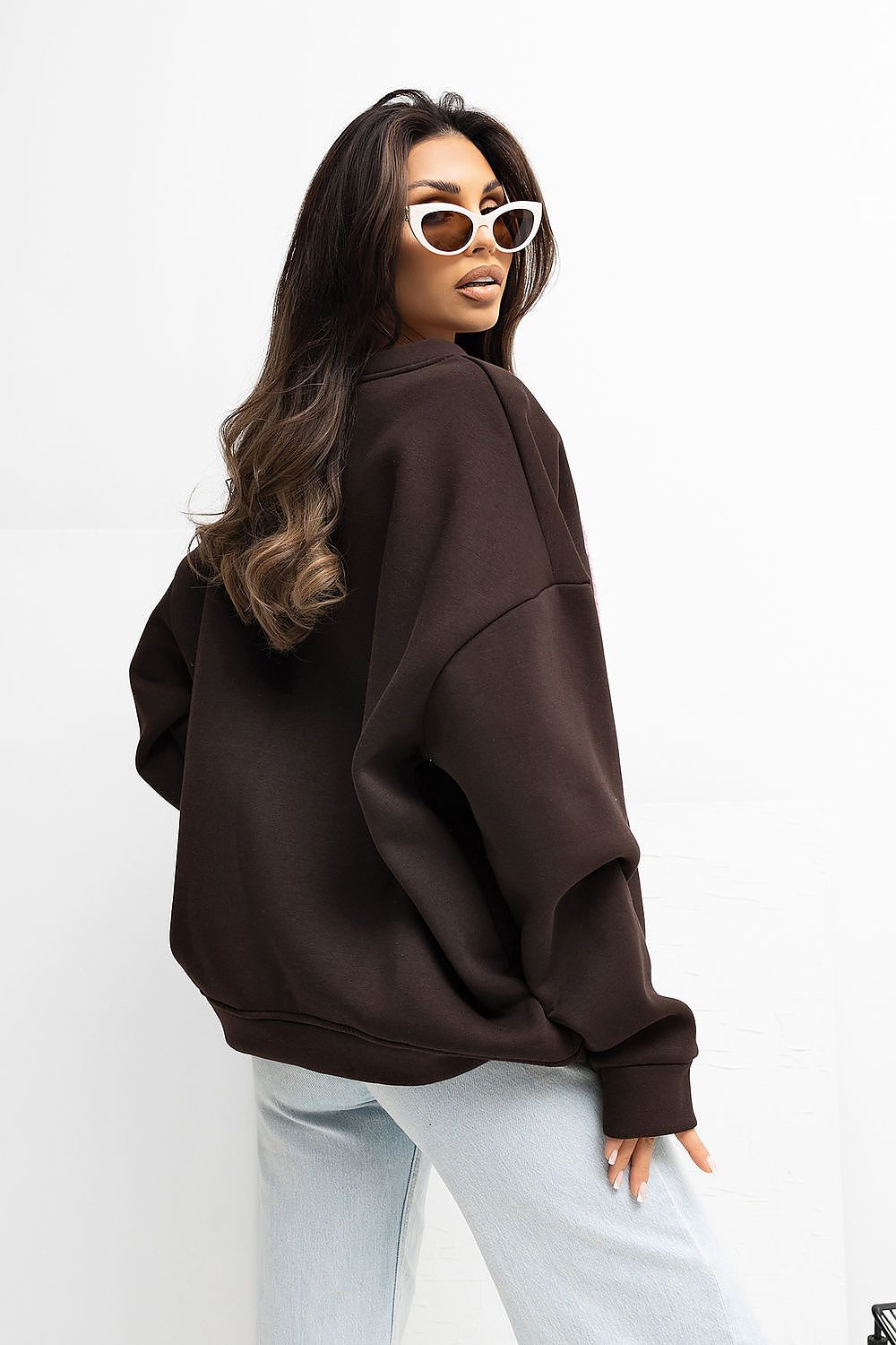 Woman wearing a brown oversized sweatshirt and light blue jeans on a white background