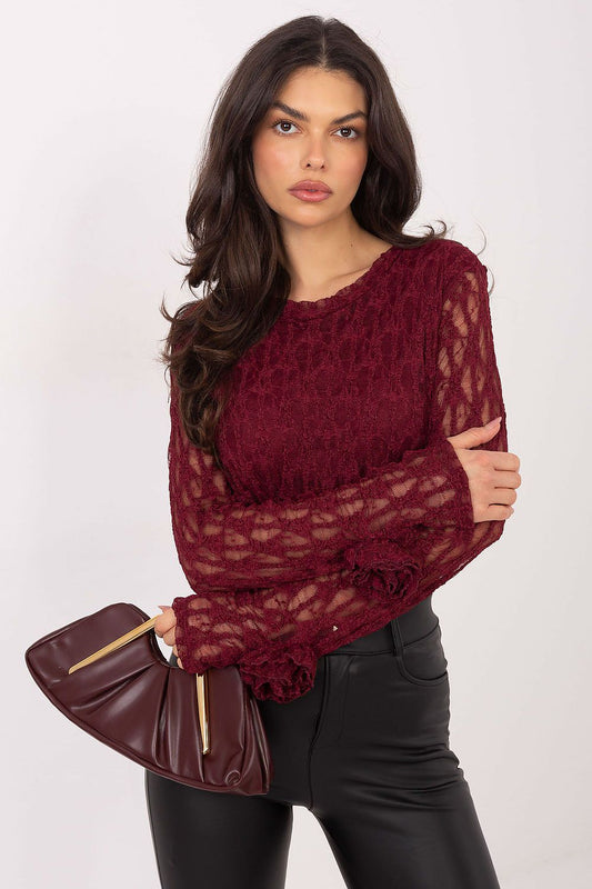 Woman wearing a burgundy lace top and holding a matching handbag against a white background