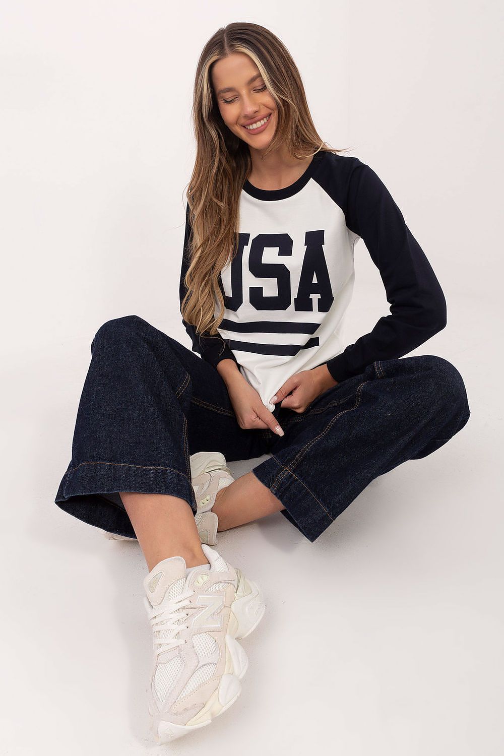 Woman wearing a 'USA' sweatshirt and jeans sitting on a white background