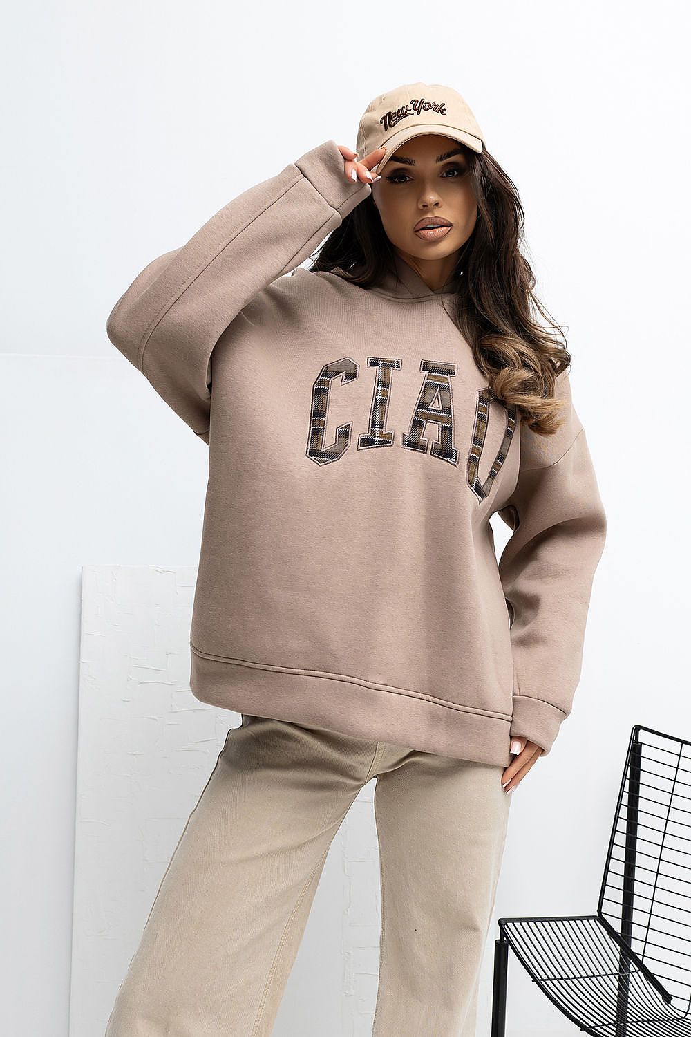 Woman wearing a beige hoodie with 'CIUD' text and matching pants, posing against a white background.