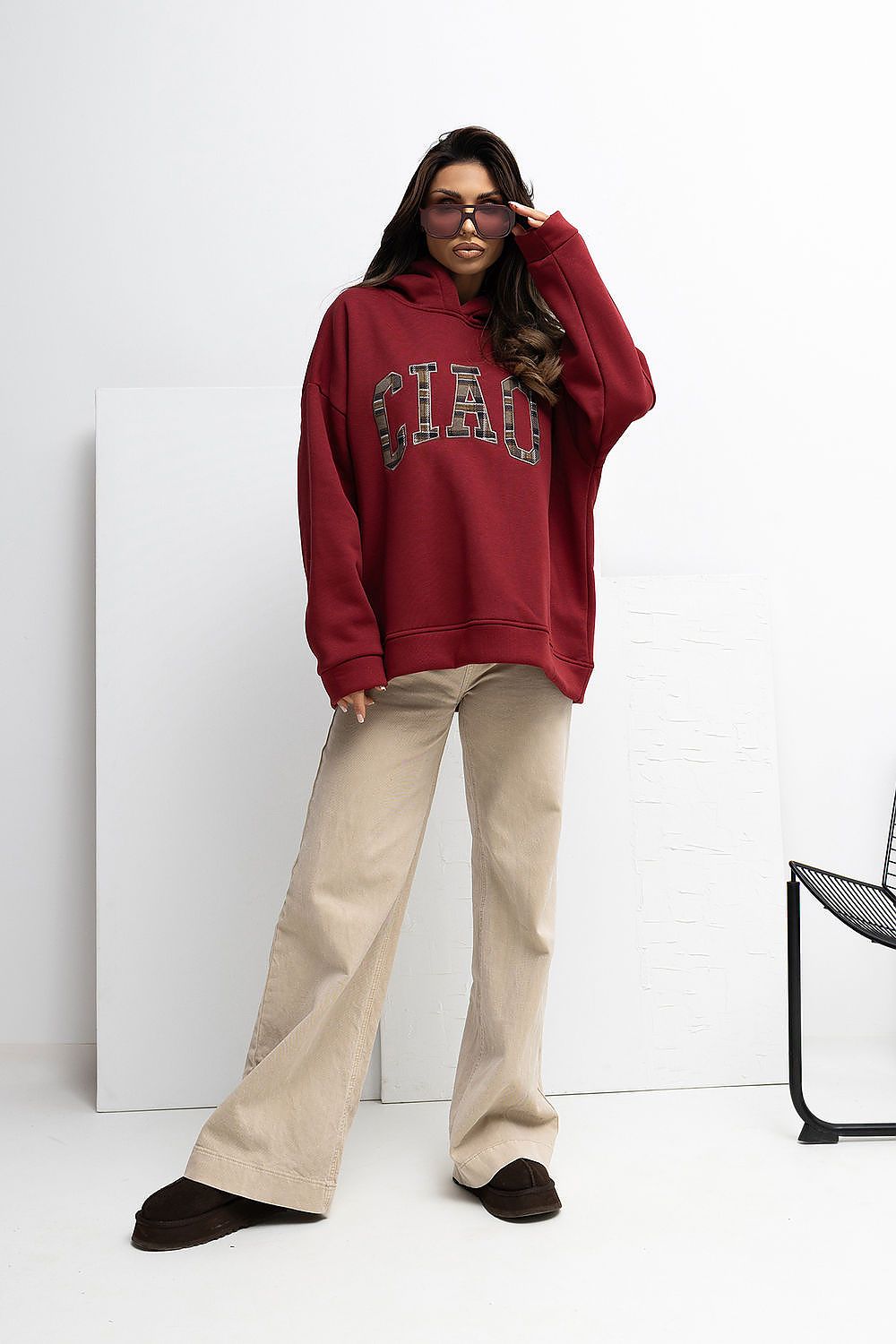 Person wearing a red hoodie with 'CIAO' text and beige pants on a white background