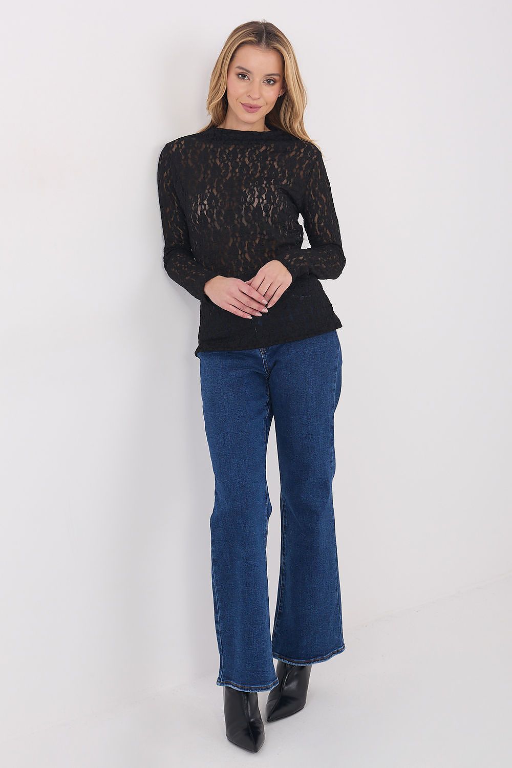 Woman wearing a black lace top and blue jeans against a white background