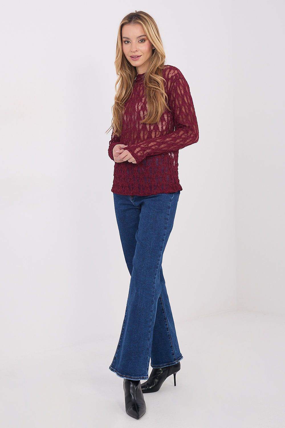 Woman wearing a burgundy lace top and blue flared jeans on a white background