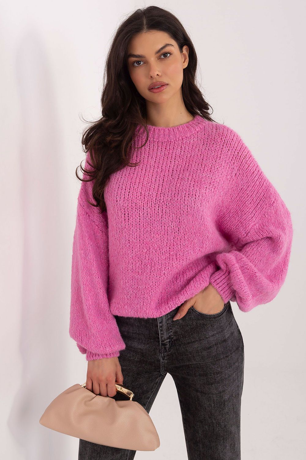 Woman wearing a pink sweater and holding a beige clutch against a white background
