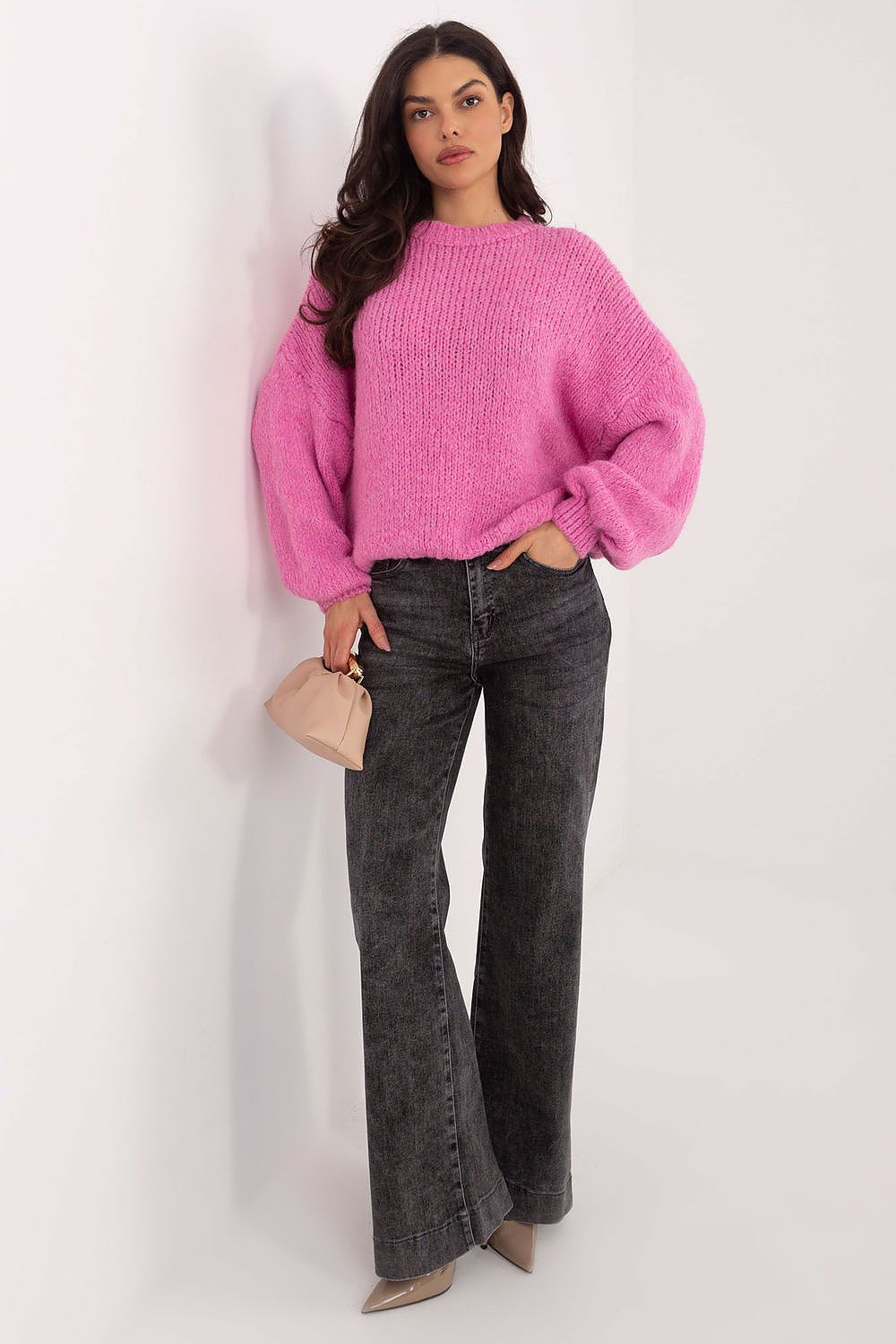 Woman wearing a pink sweater and black jeans against a white background