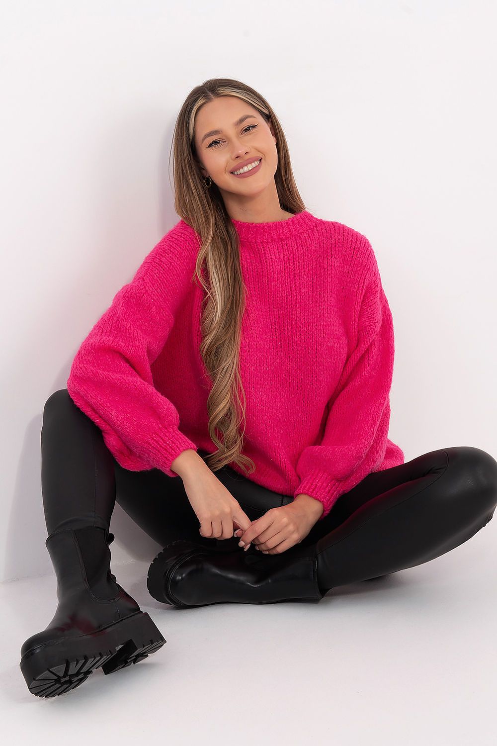 Woman wearing a bright pink sweater sitting on the floor against a white background