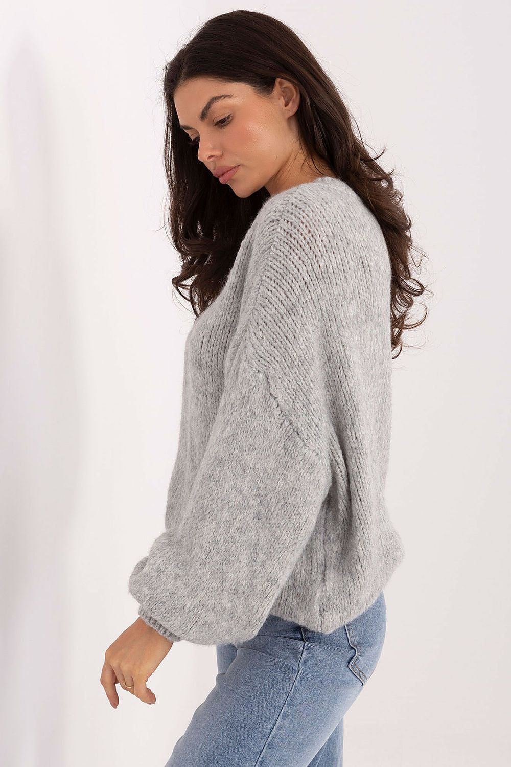 Woman wearing a gray sweater and blue jeans against a white background