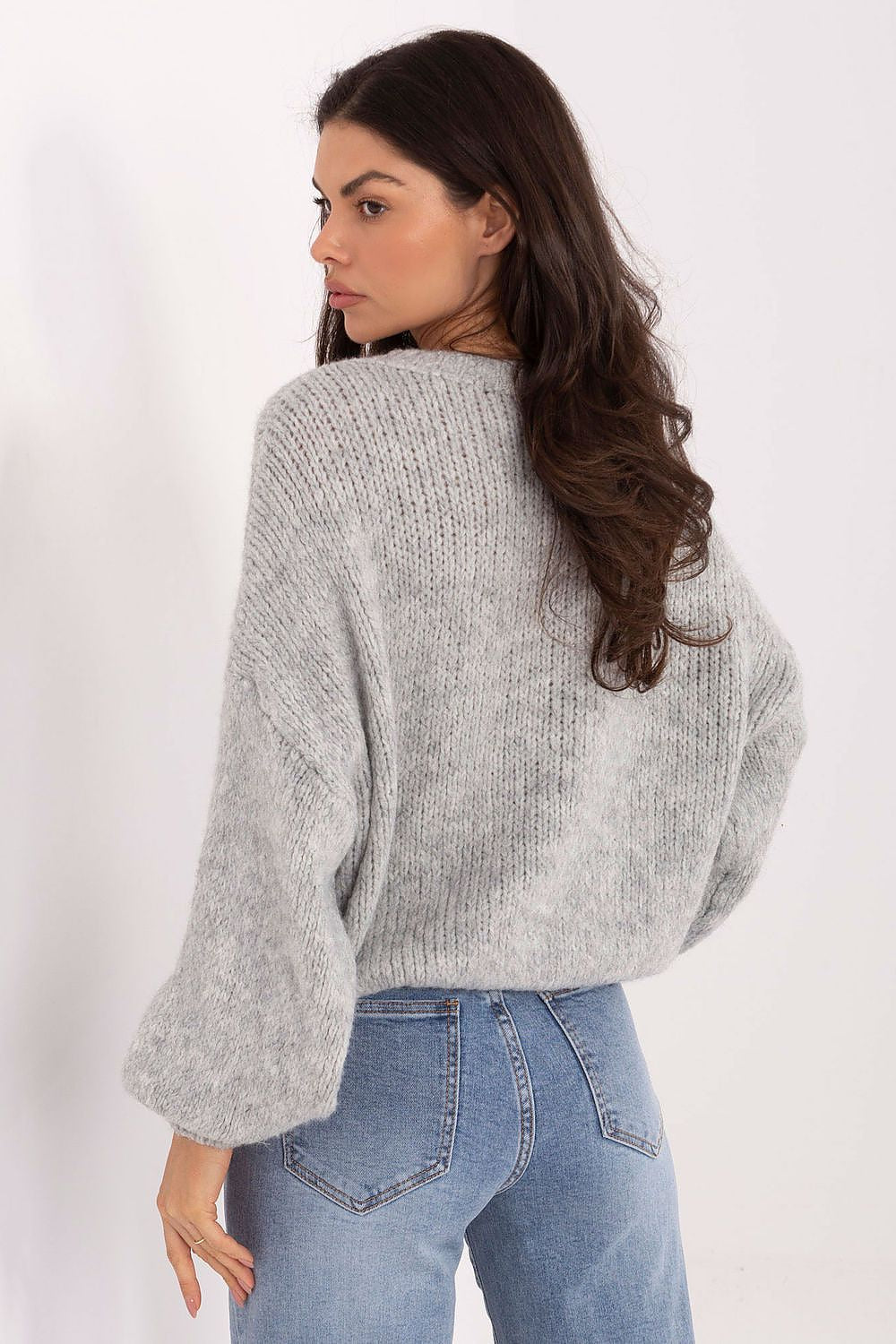 Woman wearing a gray sweater and blue jeans on a white background