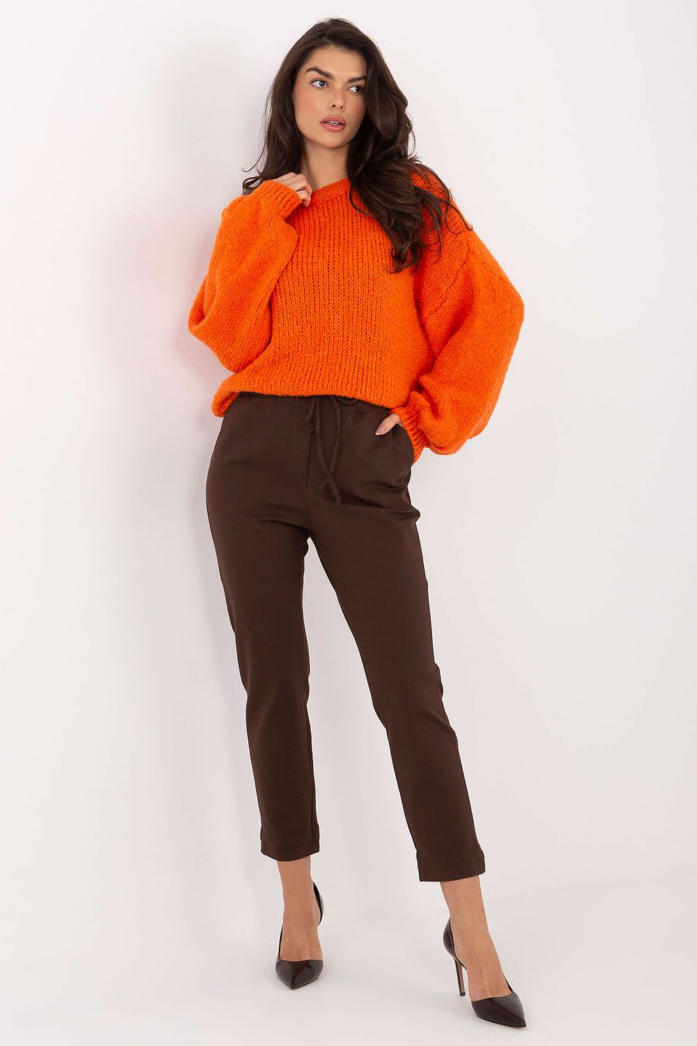 Woman wearing an orange sweater and brown pants on a white background