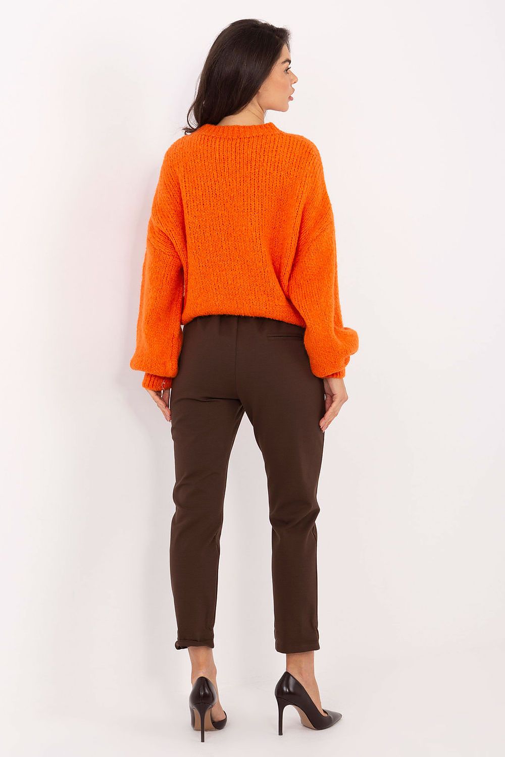 Woman wearing an orange sweater and brown pants on a white background