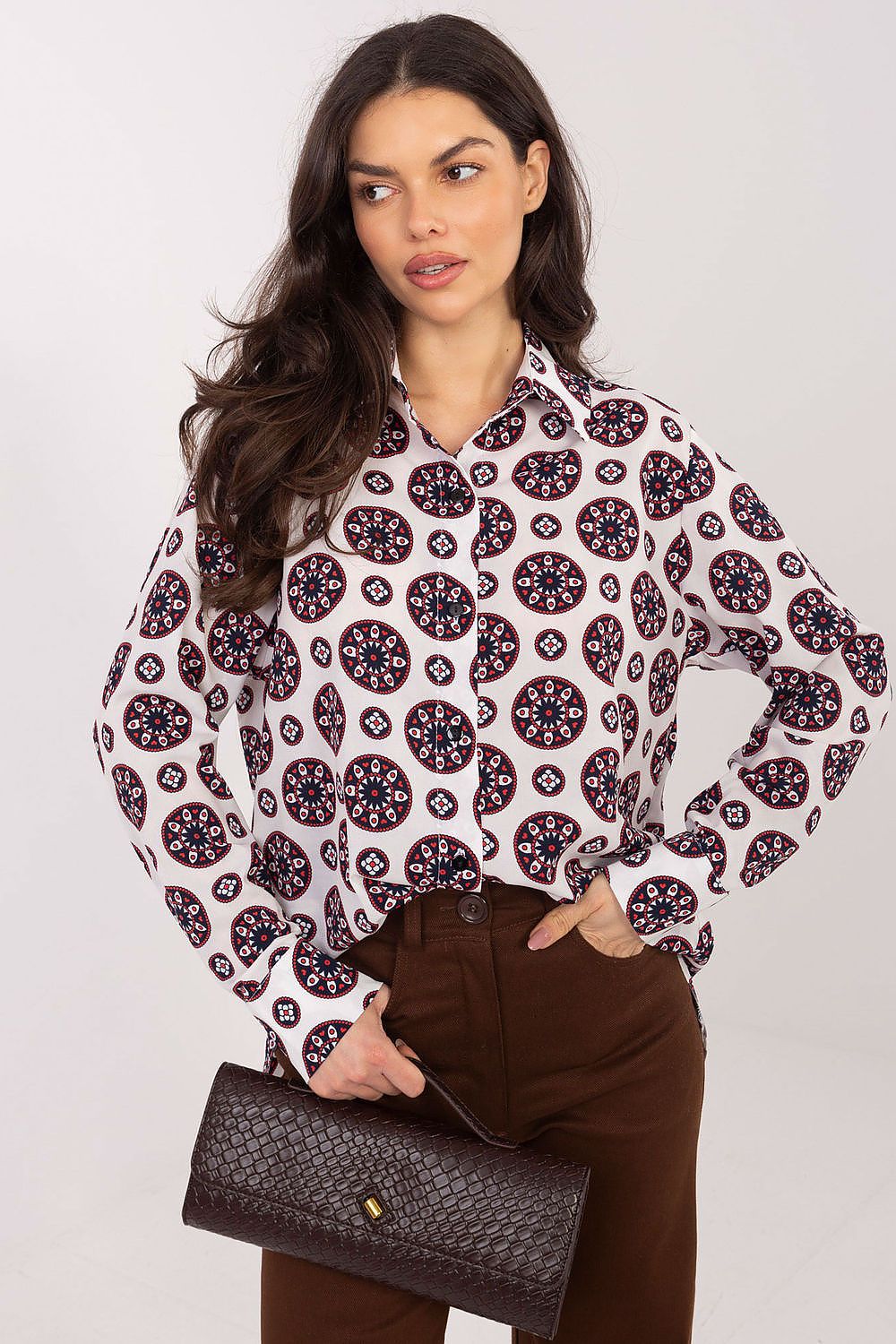 Woman wearing a patterned blouse and holding a clutch against a white background