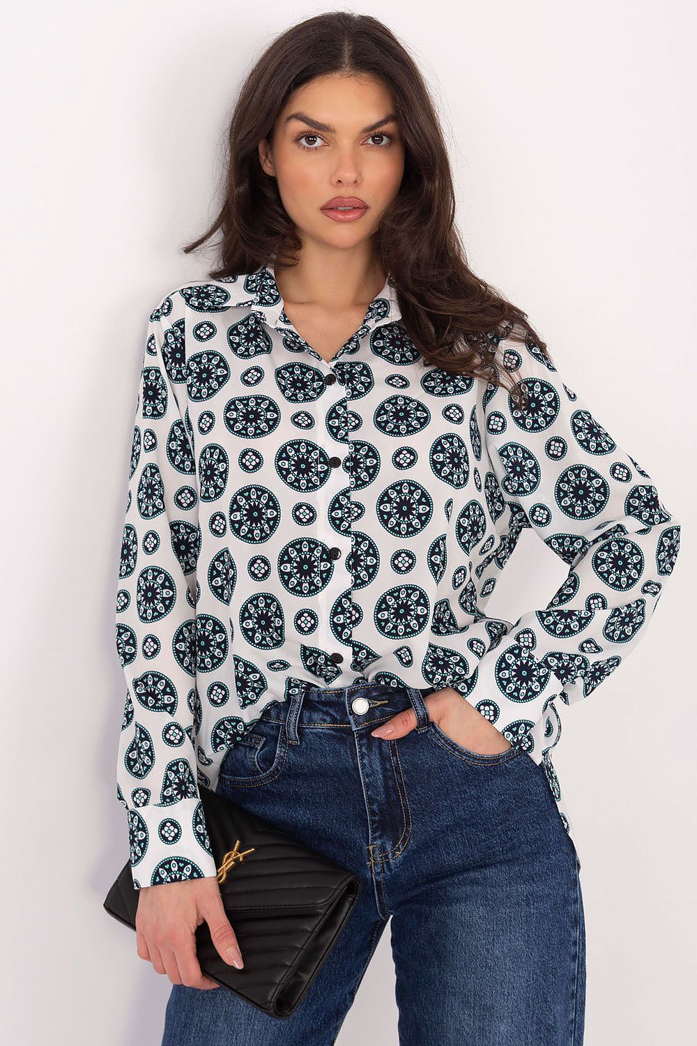 Woman wearing a patterned blouse and jeans with a black clutch against a white background