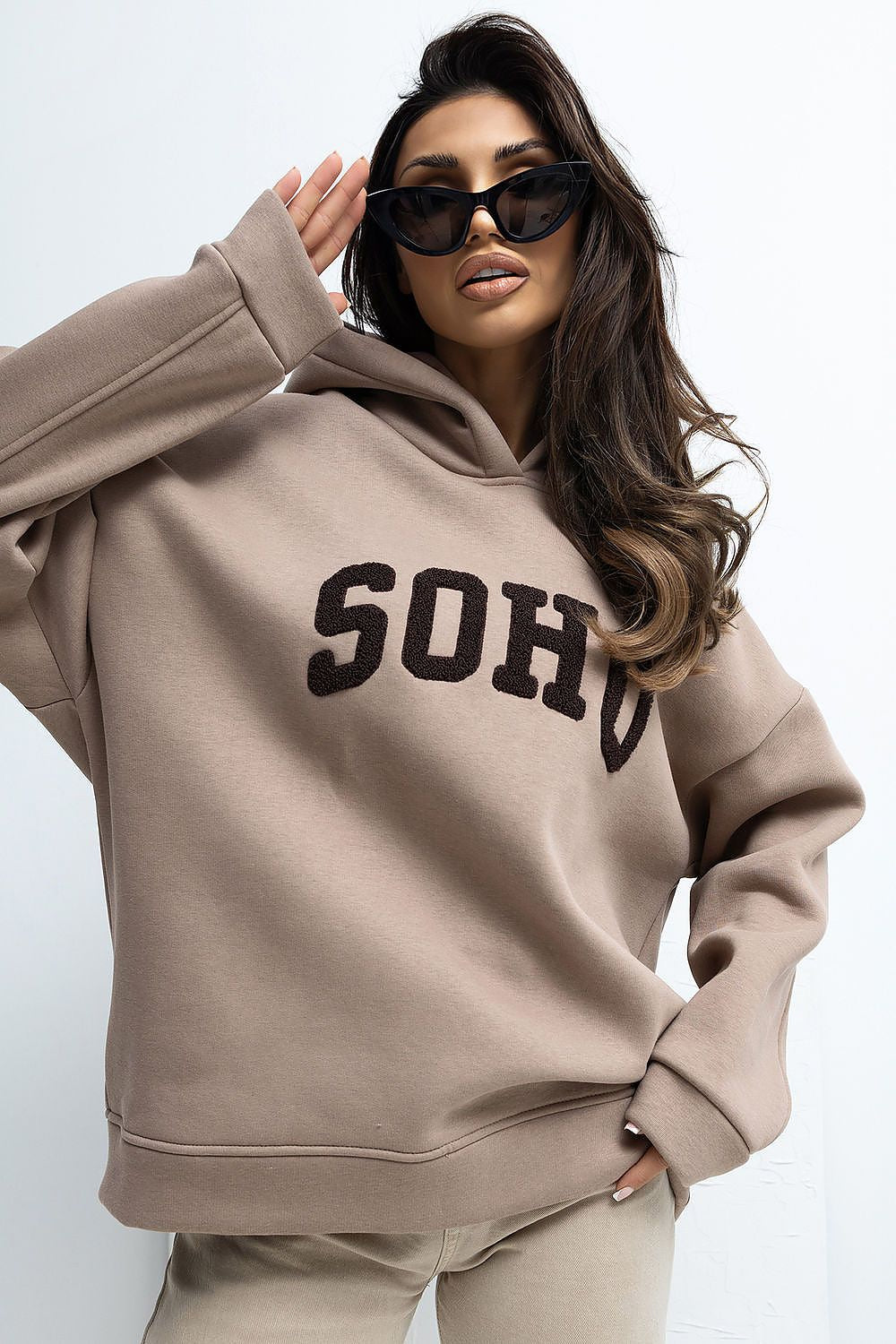 Woman wearing a beige hoodie with 'SOHO' text on a white background