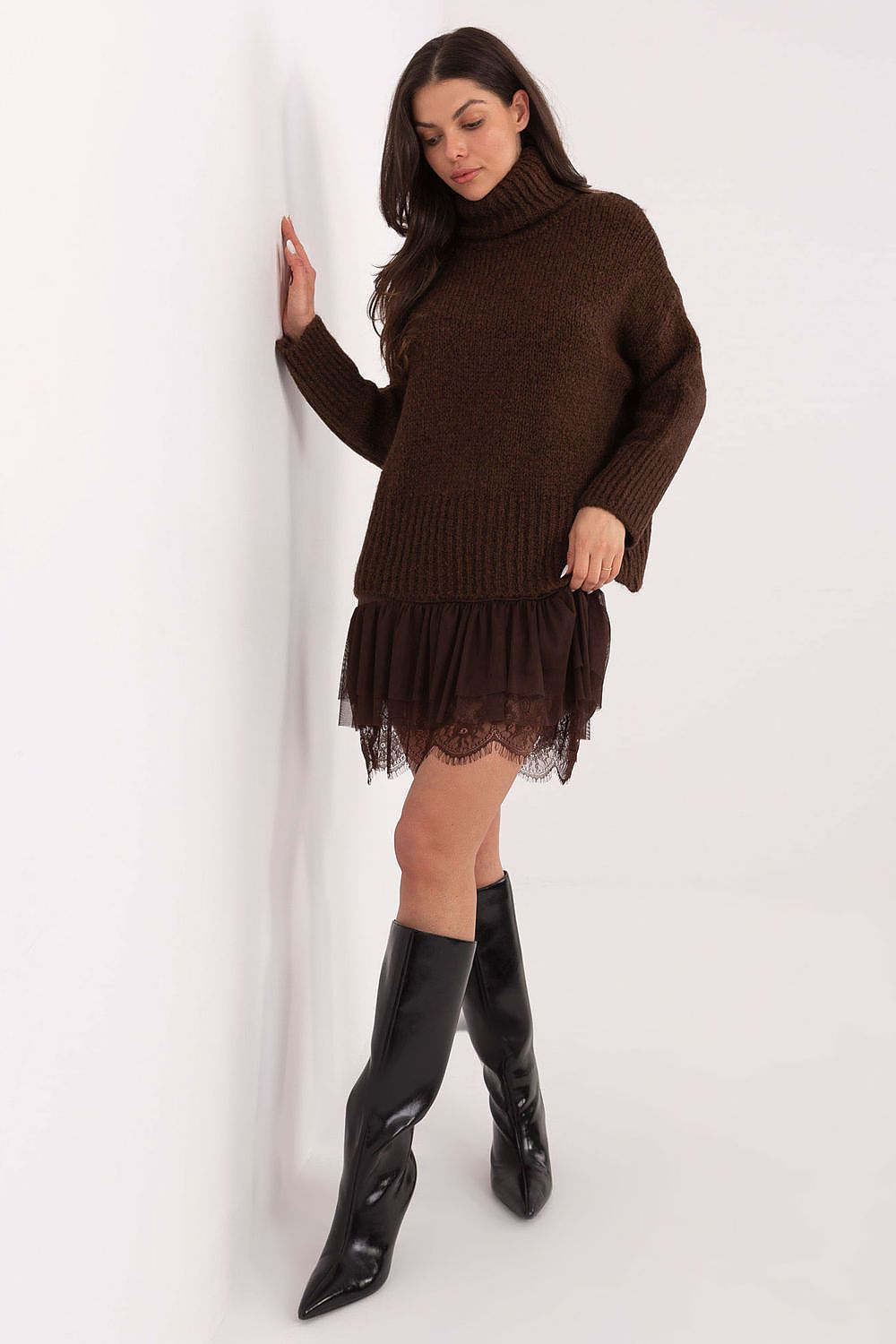 Woman wearing a brown knitted dress with a sheer overlay and black knee-high boots on a white background