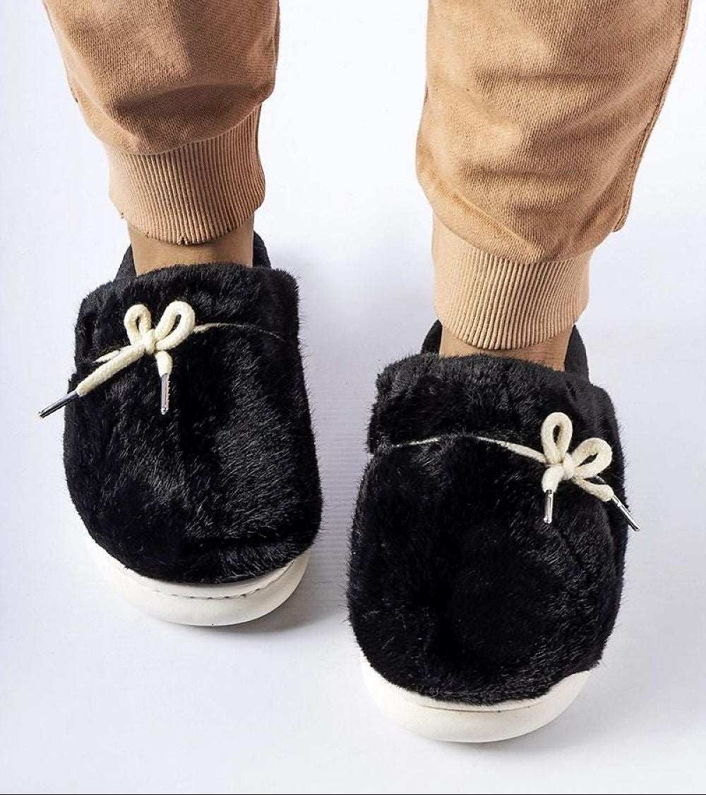 Black fuzzy slippers with white laces worn by a person on a white background