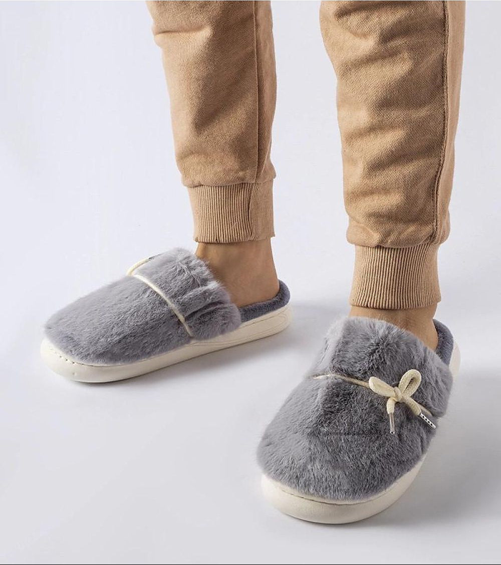 Gray slippers with fuzzy texture worn by a person in beige pants on a light gray background