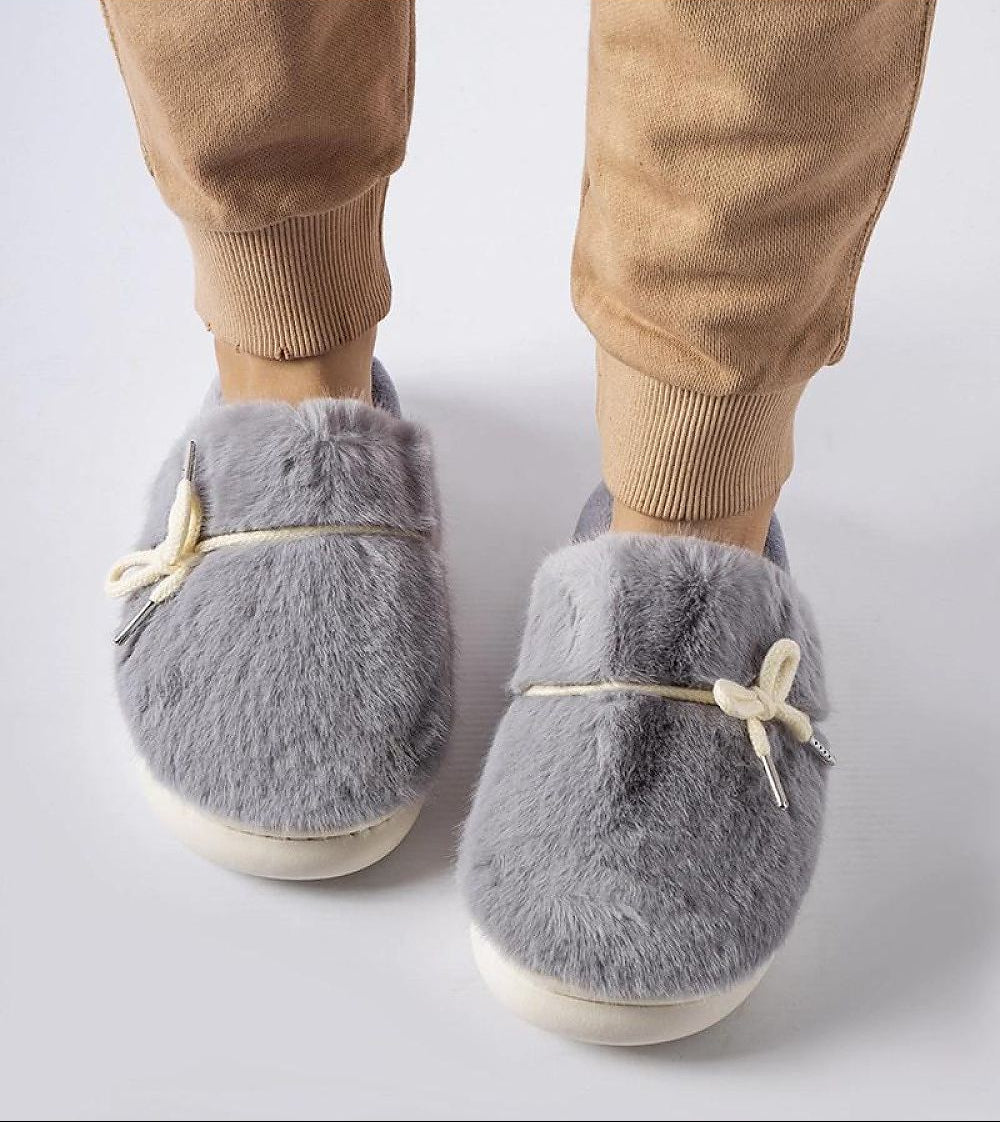Gray fuzzy slippers worn with beige pants on a light gray background