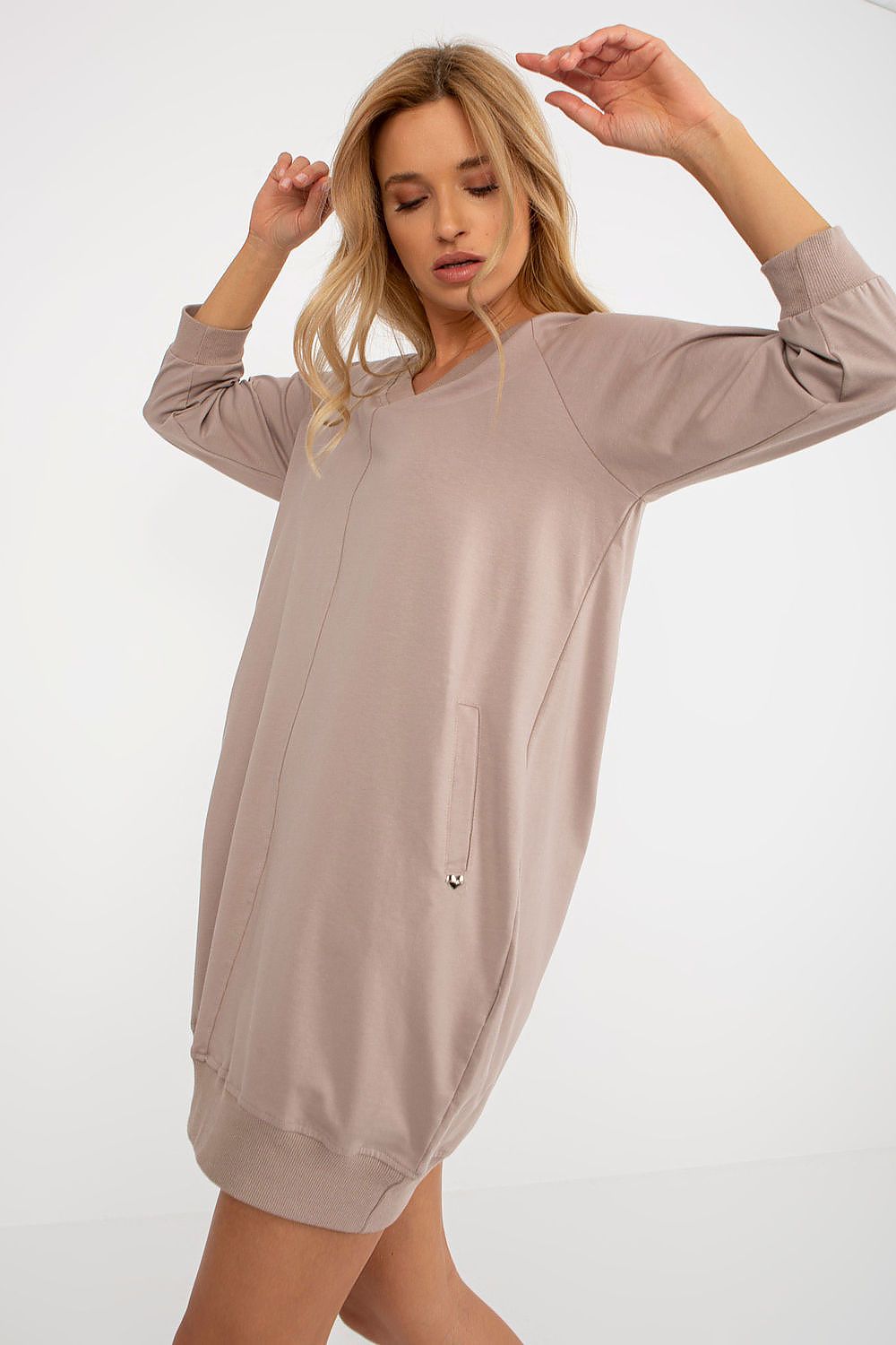 Woman wearing a beige long-sleeve dress against a white background