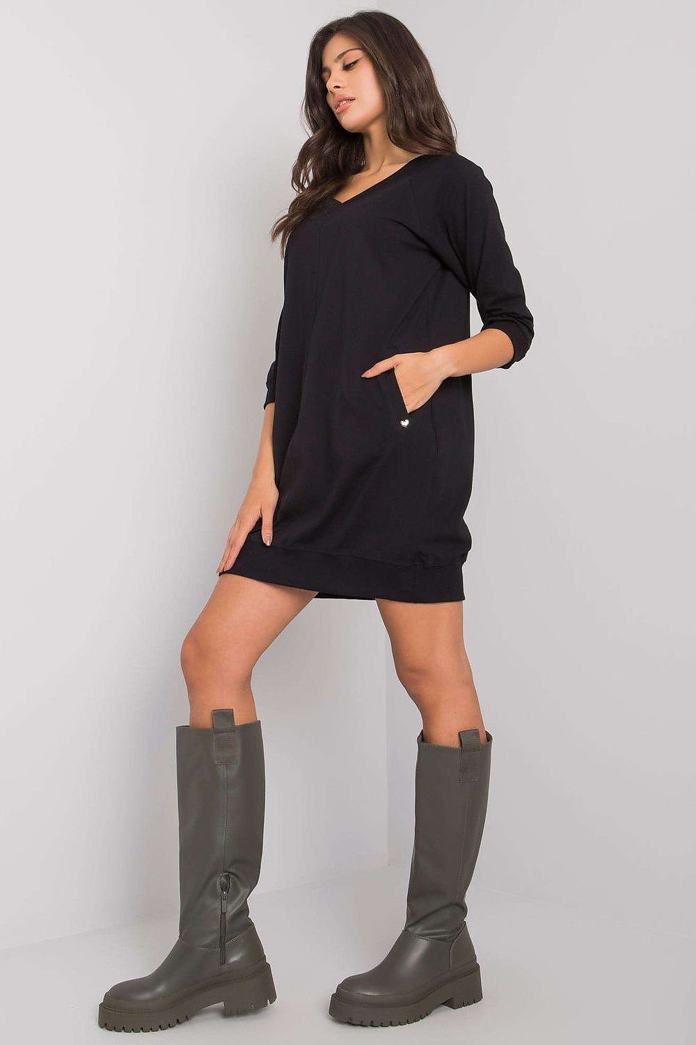 Woman wearing a black dress and green boots on a plain background