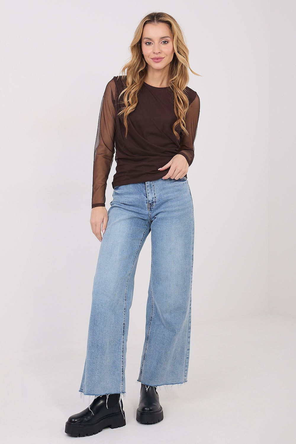 Woman wearing a brown mesh top and blue jeans on a white background