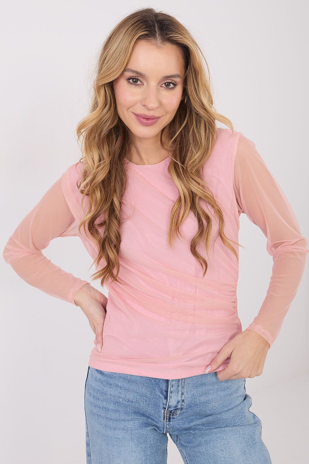 Woman wearing a pink long-sleeve top and blue jeans on a white background