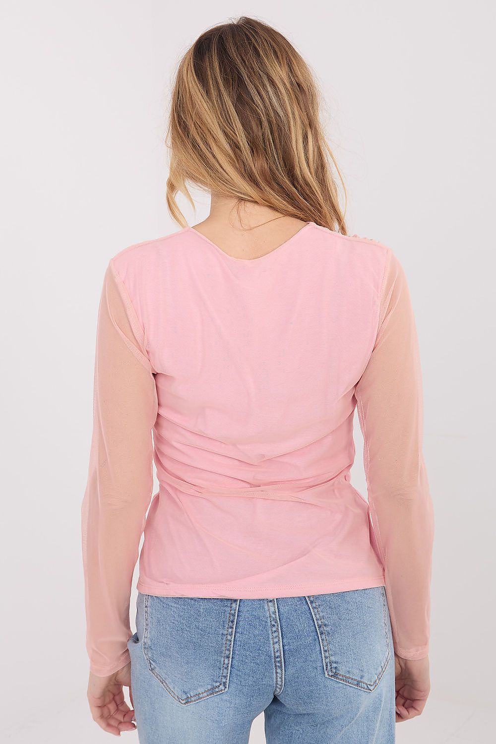 Person wearing a pink long-sleeve top and blue jeans on a plain background