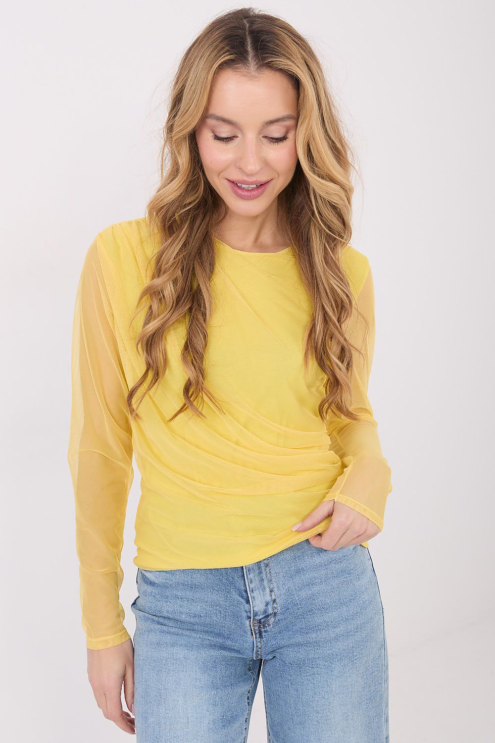 Woman wearing a yellow long-sleeve top and blue jeans on a white background