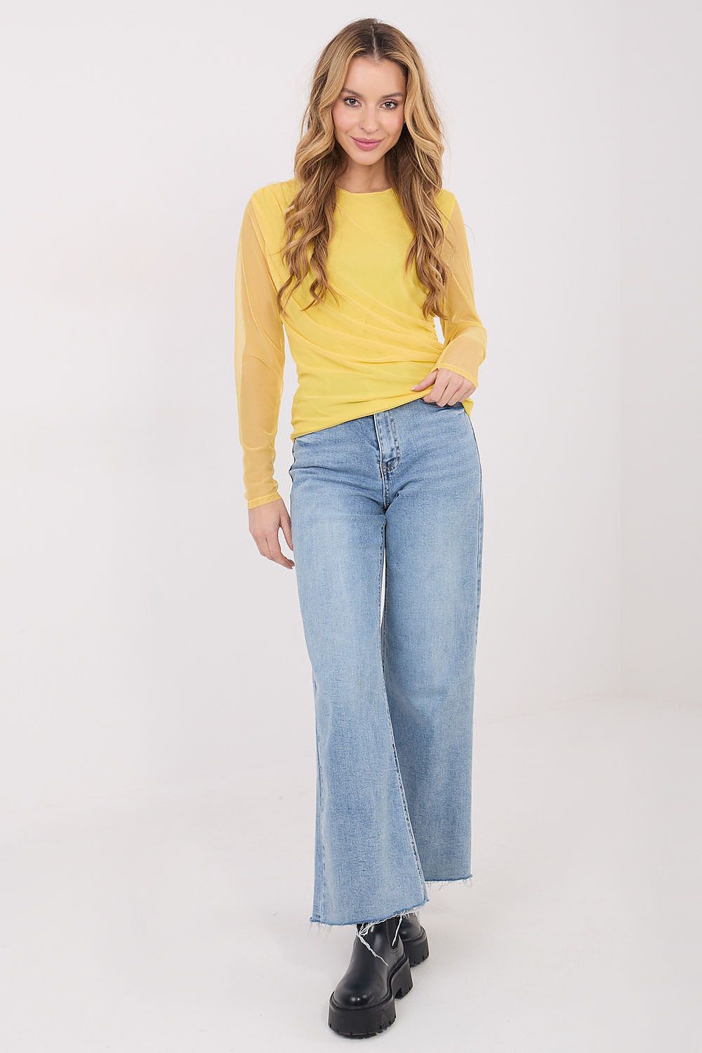 Woman wearing a yellow long-sleeve top and light blue jeans on a white background