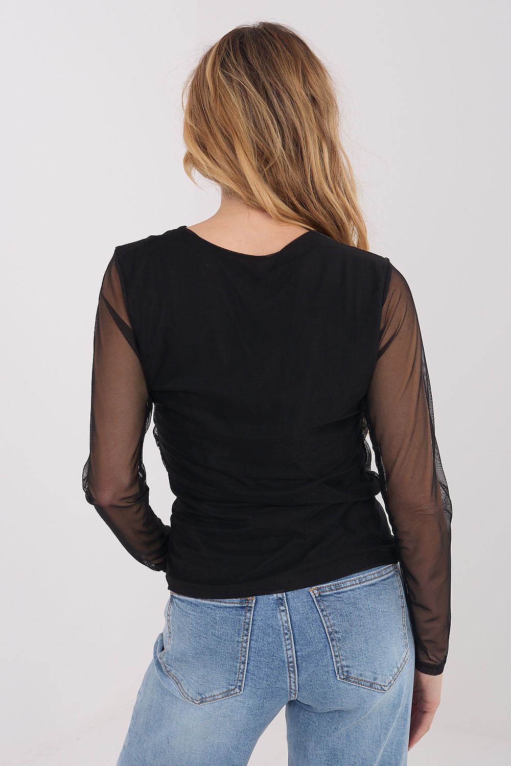 Person wearing a black top with sheer sleeves and blue jeans on a white background