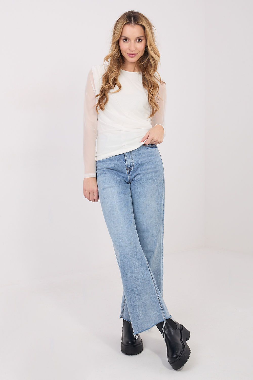 Woman wearing a white top, light blue jeans, and black shoes on a white background