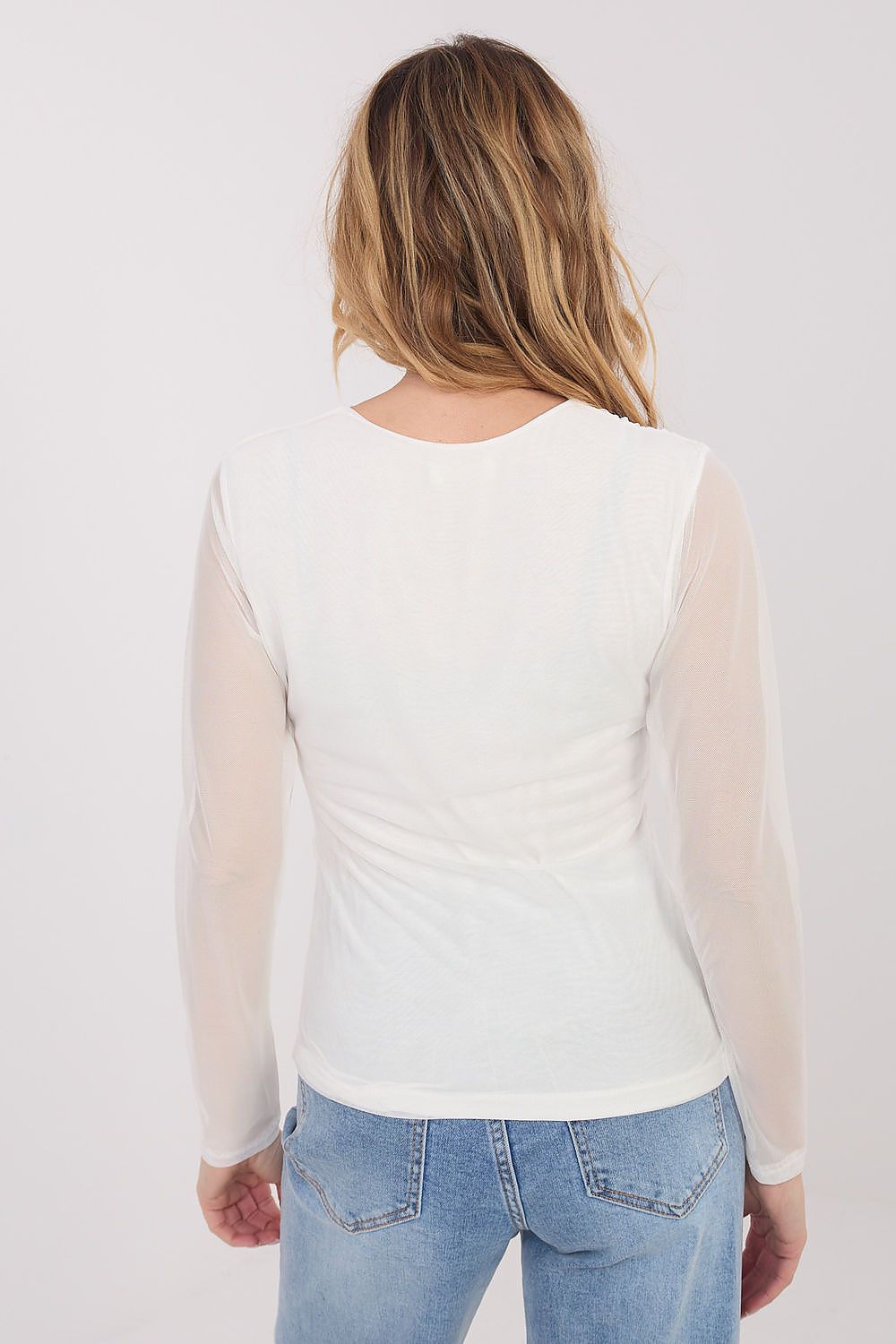 Person wearing a white long-sleeve top with sheer sleeves and blue jeans on a light gray background