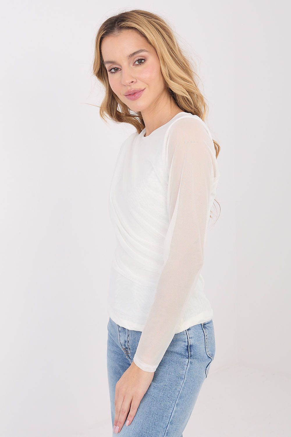 Woman wearing a white long-sleeve top and blue jeans on a plain background