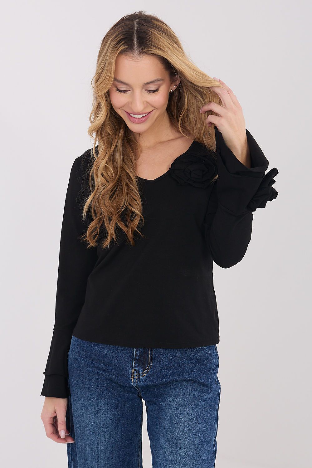 Woman wearing a black top with ruffled sleeves and blue jeans on a white background