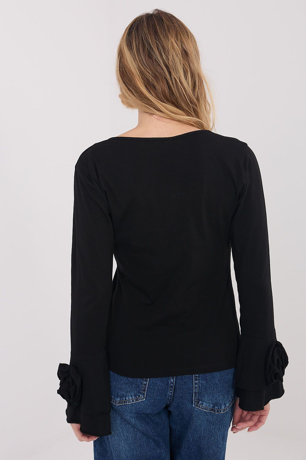 Person wearing a black long-sleeve top with ruffled cuffs on a plain background