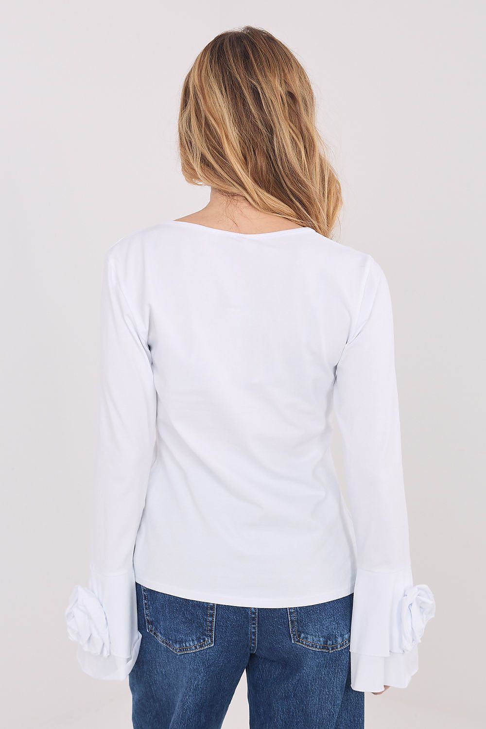 Person wearing a white long-sleeve top and blue jeans with white gloves on a plain background