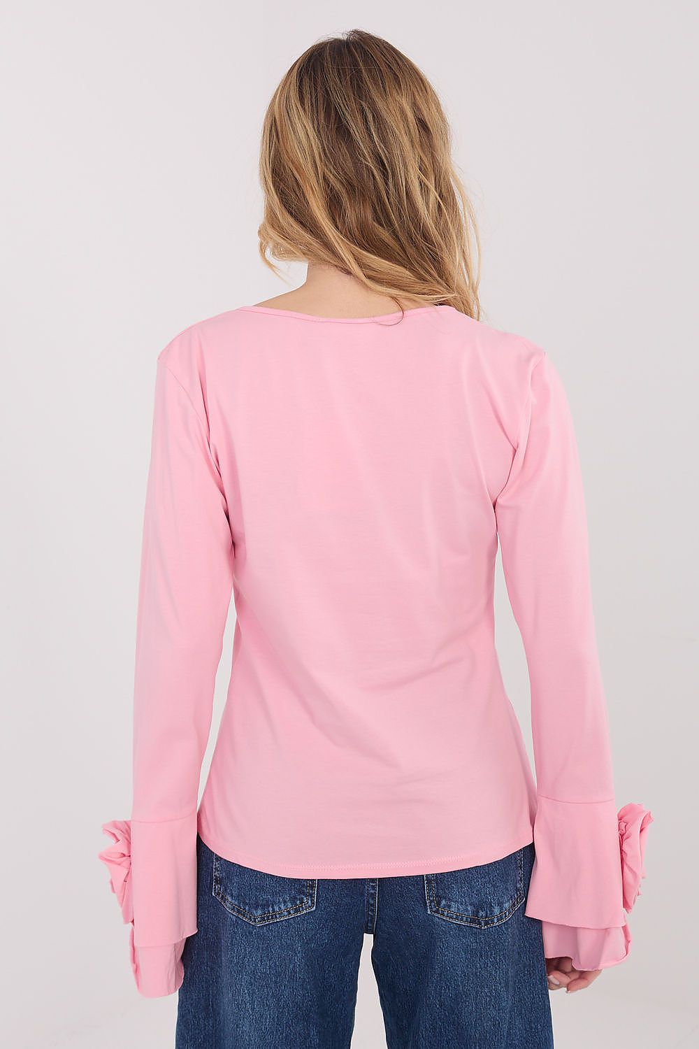 Person wearing a pink long-sleeve top with ruffled sleeves on a plain background