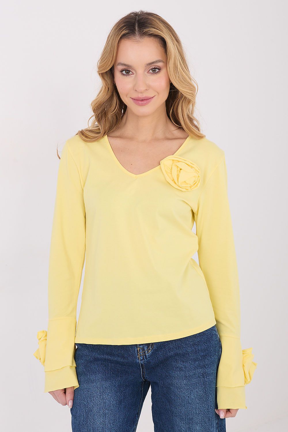 Woman wearing a yellow long-sleeve top with a flower detail on a white background