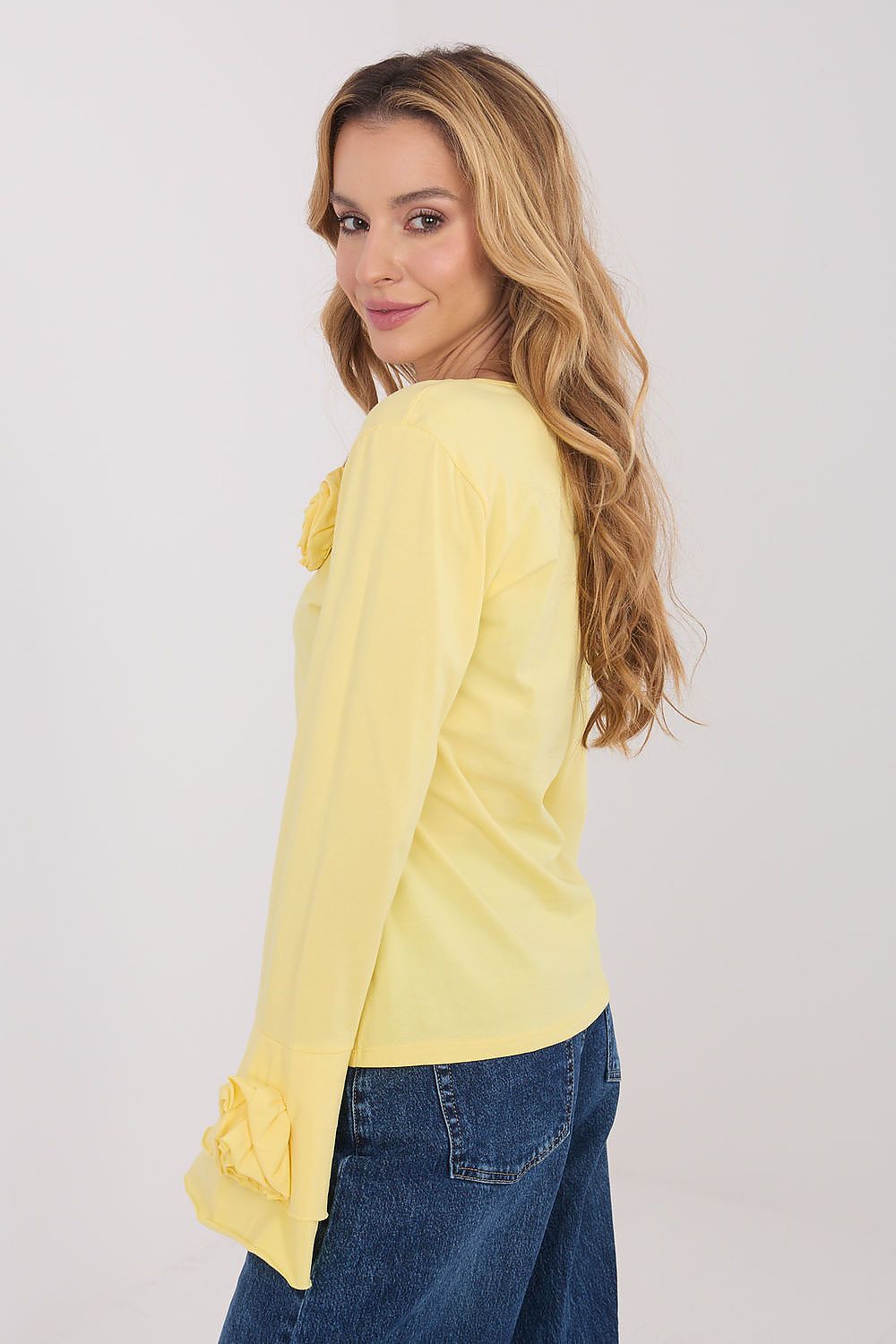 Woman wearing a yellow blouse with ruffled sleeves and blue jeans on a white background