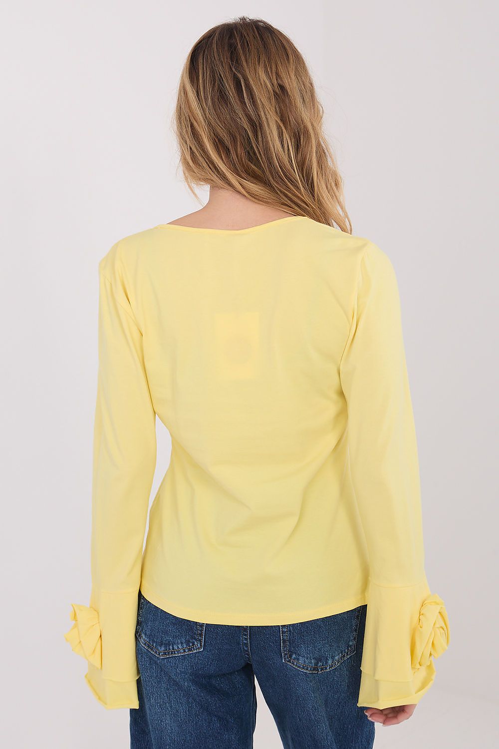 Woman wearing a yellow long-sleeve top with blue jeans on a white background