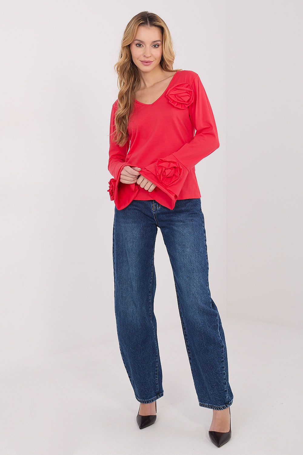 Woman wearing a red blouse with floral details and blue jeans on a white background