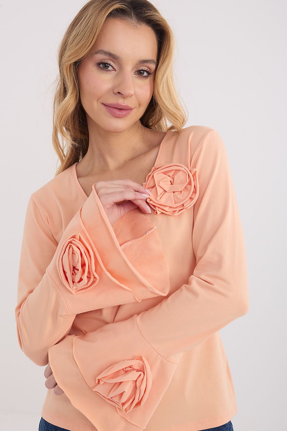 Woman wearing a peach-colored blouse with floral embellishments on a white background