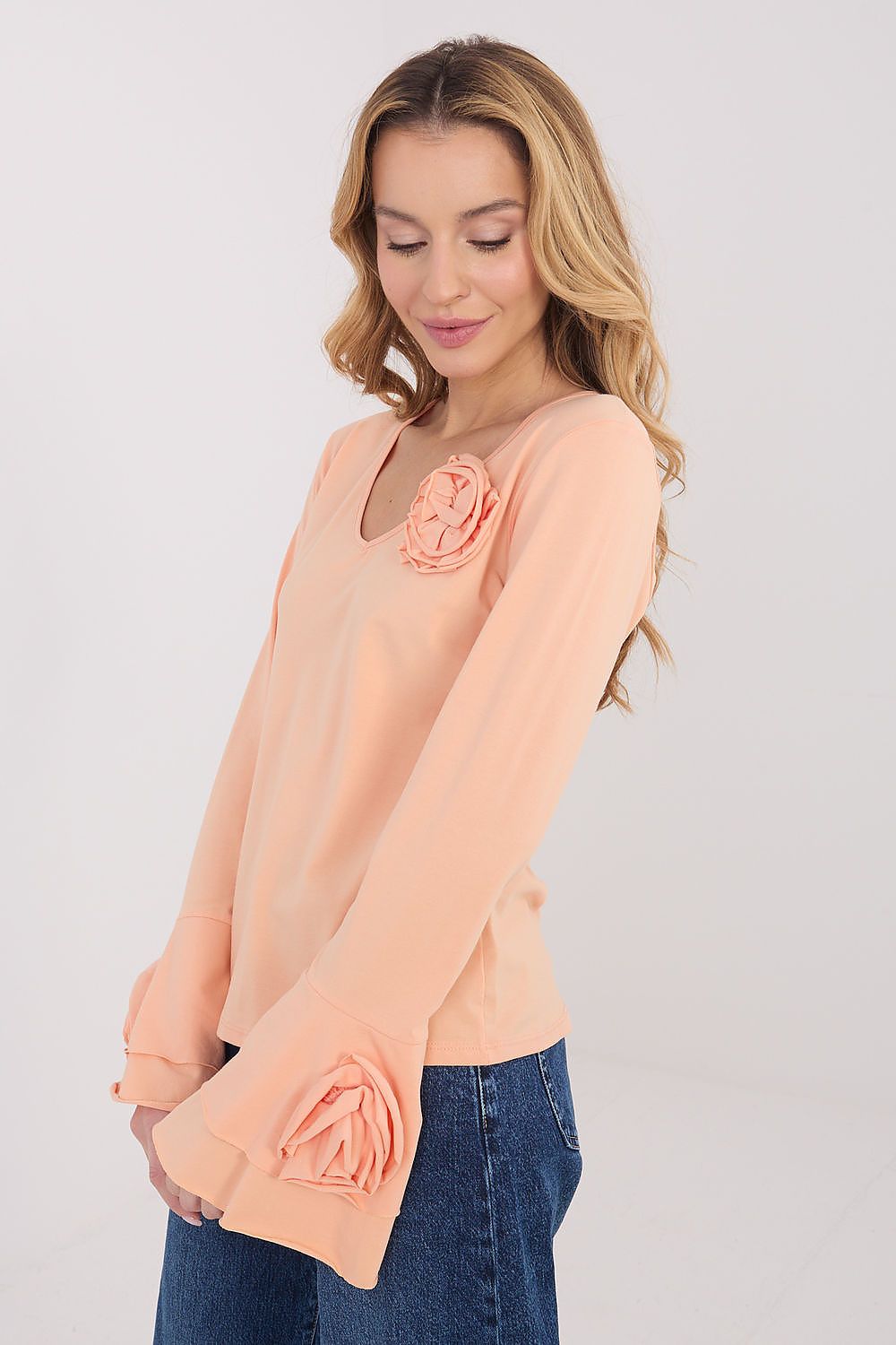 Woman wearing a peach blouse with floral details on a plain background