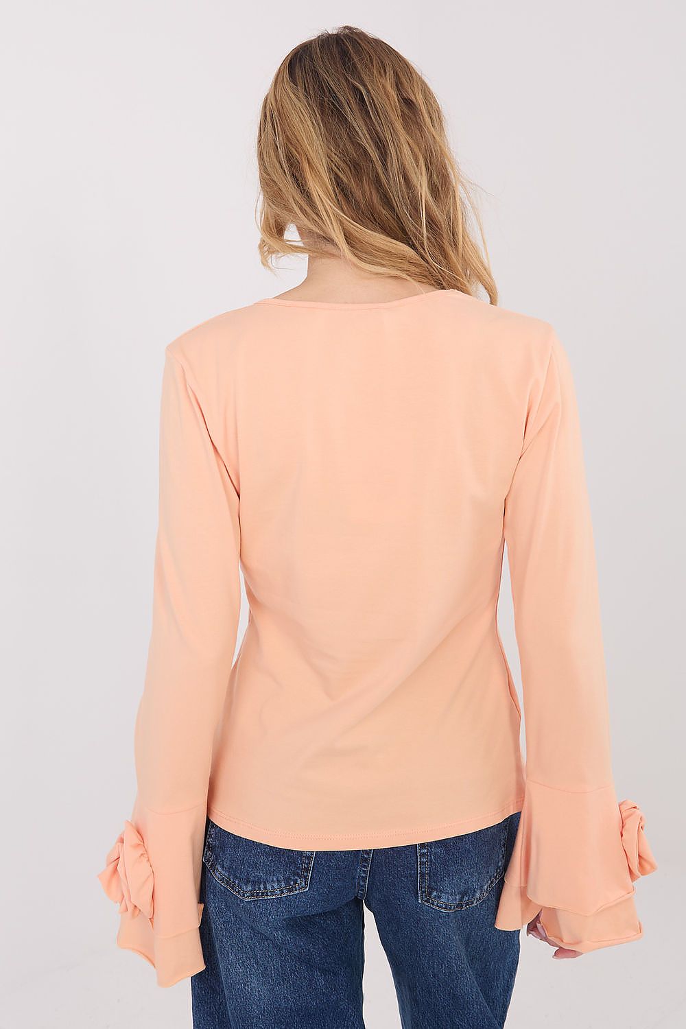 Person wearing a peach long-sleeve top and blue jeans on a plain background